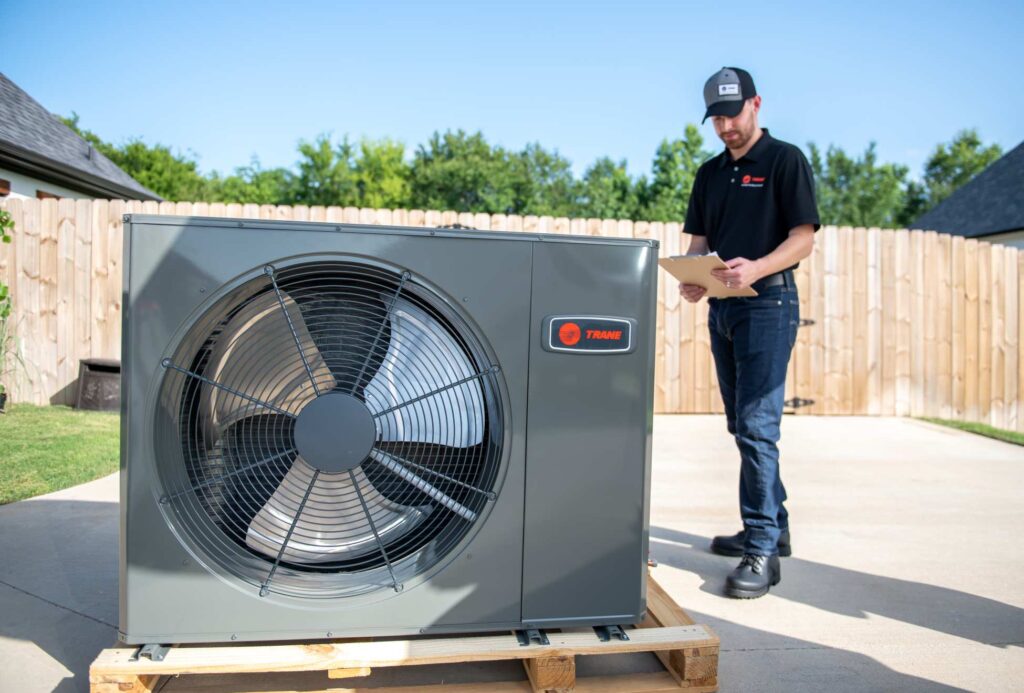 Trane technician inspecting a newly delivered Trane outdoor unit on a wooden pallet in a residential driveway